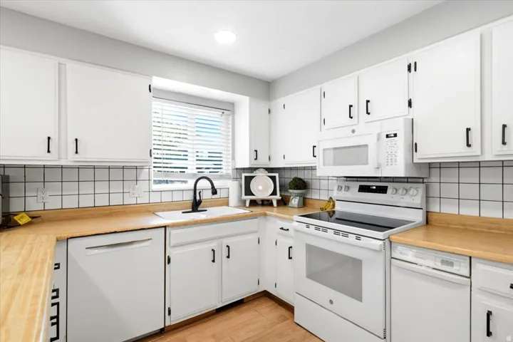 Kitchen featuring white cabinetry with black hardware, wood-finish countertops, and a white tile backsplash