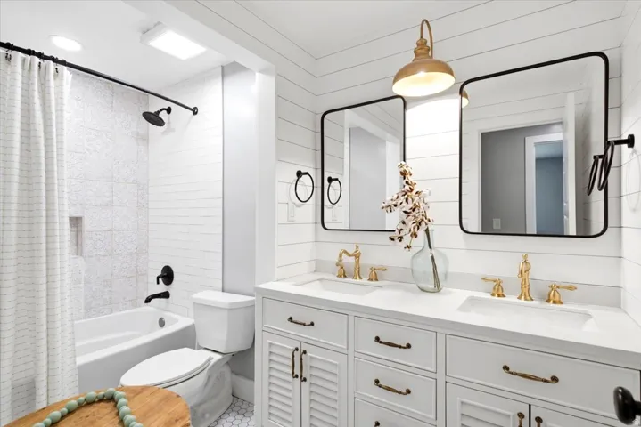 Double vanity with white cabinetry, gold-tone fixtures, and rectangular mirrors