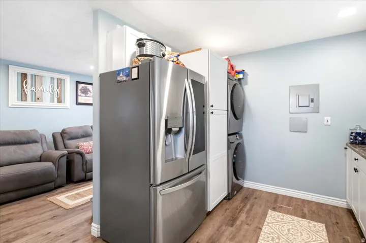 Laundry area with wood-finish flooring, white cabinetry, and a stacked washer and dryer