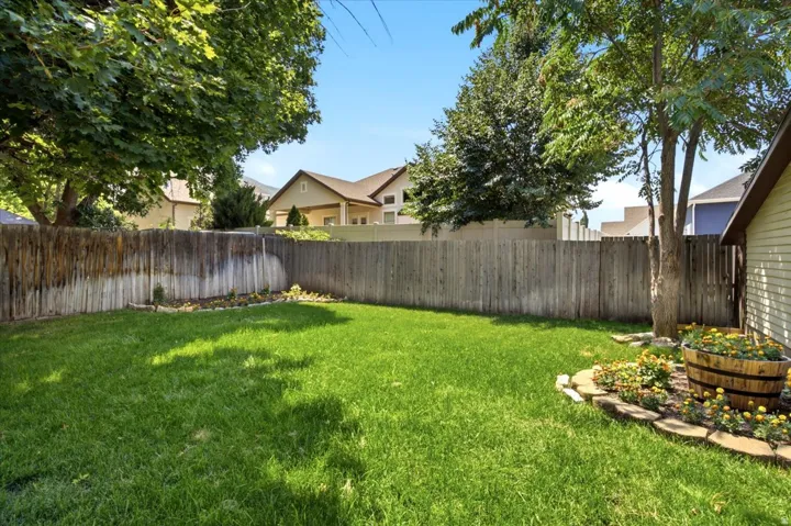 Expansive backyard featuring a lush green lawn, mature trees, a privacy fence, and a decorative planter