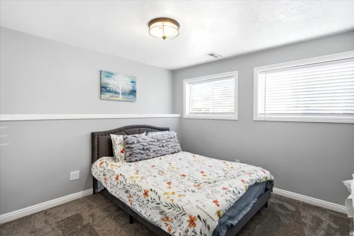 Bedroom featuring two windows with blinds, gray walls, white baseboards, and a semi-flush mount ceiling light
