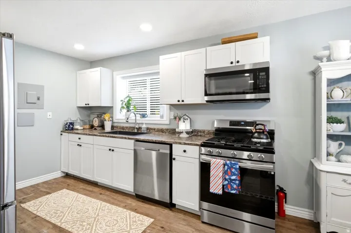 Kitchen featuring white cabinetry, stainless steel appliances, a dark sink, wood-finish flooring, and recessed lighting