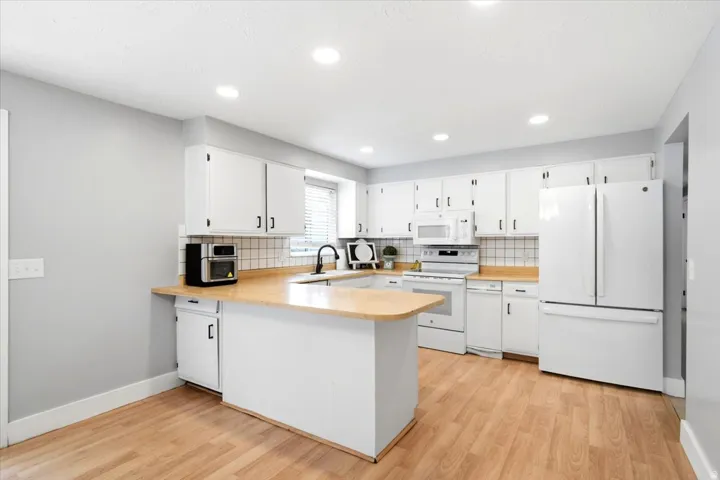 Kitchen featuring wood-finish flooring, white cabinetry, light wood-finish countertops, white appliances, and recessed lighting