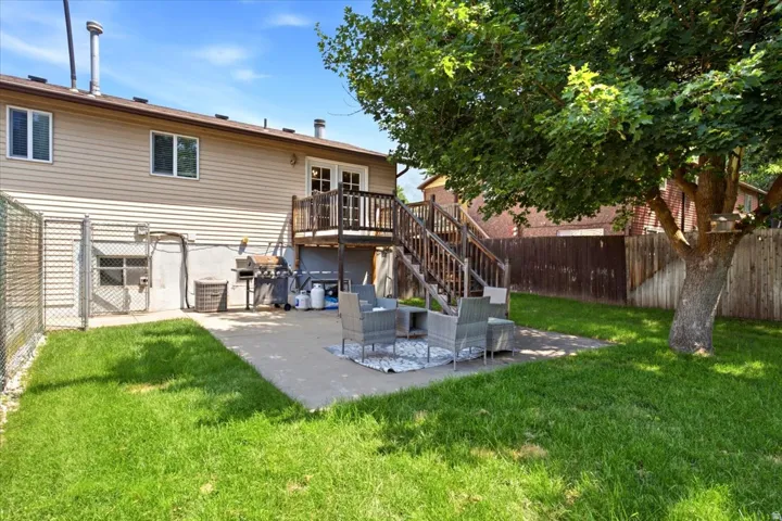 Rear exterior featuring a spacious lawn, concrete patio, and a mature shade tree