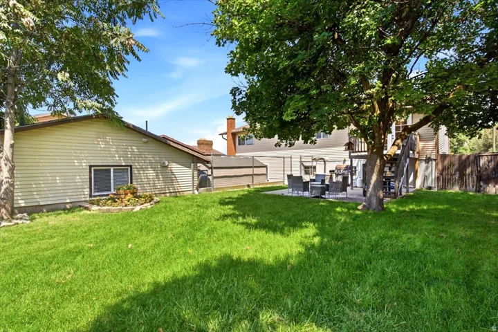 Spacious backyard featuring a large tree, expansive lawn area, and a concrete patio