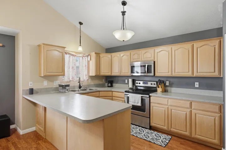Open-concept kitchen featuring wood-finish flooring, light wood cabinetry, and a peninsula countertop