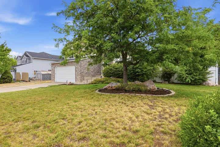 Front exterior featuring a brick facade, white garage door, concrete driveway, and mature landscaping with a large tree and decorative rocks