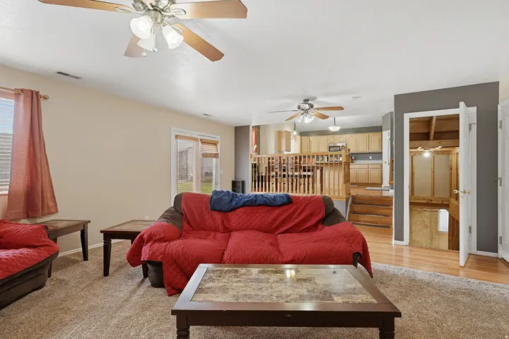 Open-concept living space featuring neutral carpet flooring, two ceiling fans with integrated lighting, and a sliding glass door providing outdoor access