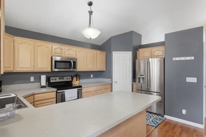 Kitchen featuring light wood cabinetry, stainless steel appliances, a built-in microwave, and a breakfast bar