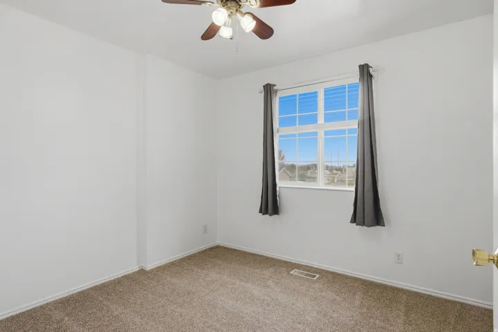Neutral palette room featuring a window with a neighborhood backdrop, carpet flooring, and a ceiling fan with integrated lighting
