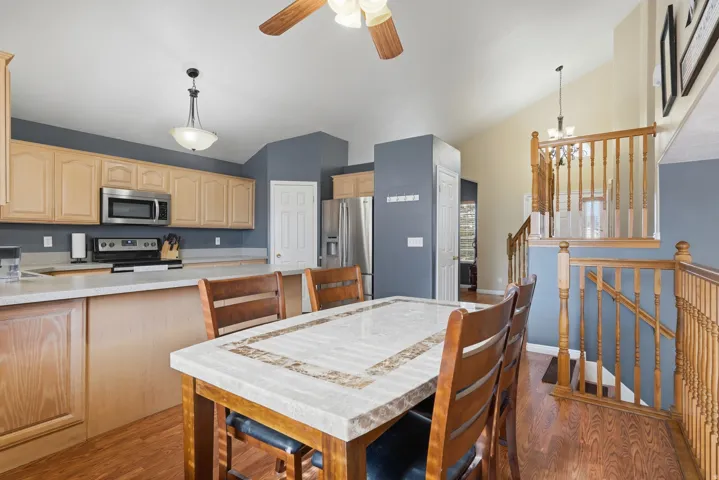 Open-concept kitchen and dining area featuring wood-finish flooring, light wood cabinetry, stainless steel appliances, and light-toned countertops