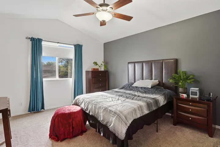 Vaulted ceiling bedroom with a ceiling fan, plush carpeting, and a window with natural light