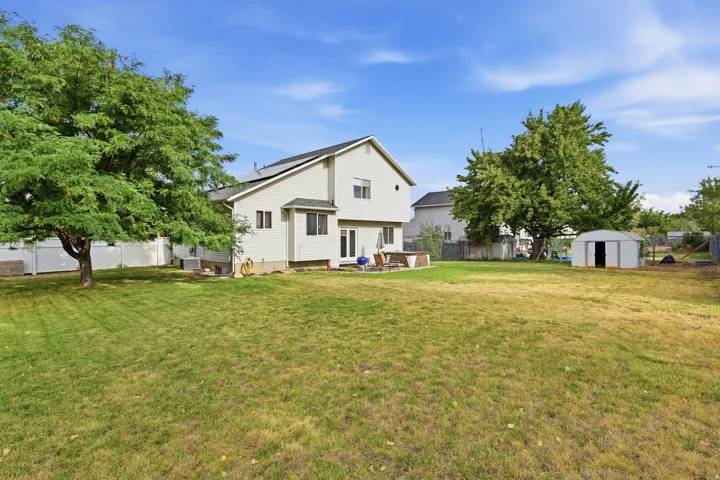 Expansive backyard featuring a large green space, mature trees, a white vinyl privacy fence, and a storage shed