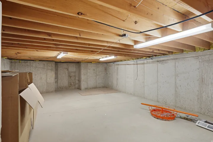 Unfinished basement with exposed wood ceiling joists and concrete walls