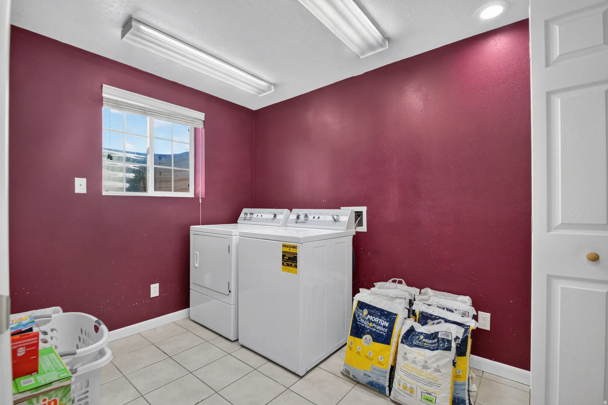 Utility room featuring a window with white blinds, tile flooring, and overhead fluorescent lighting