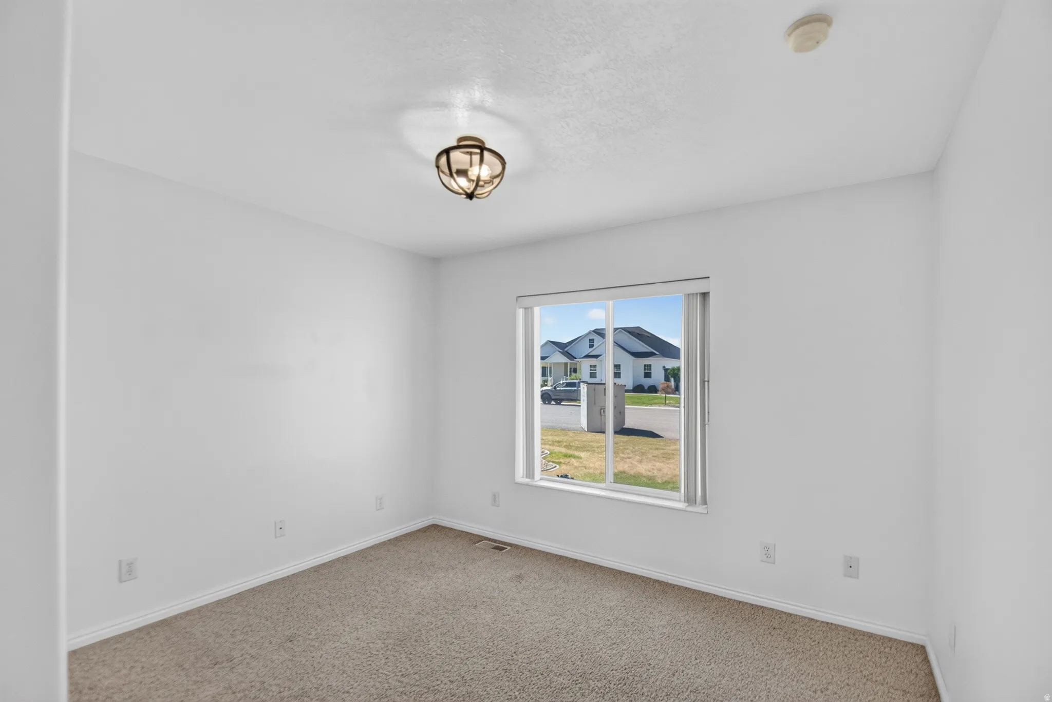 Carpeted room featuring a single window, white walls, and a ceiling-mounted light fixture