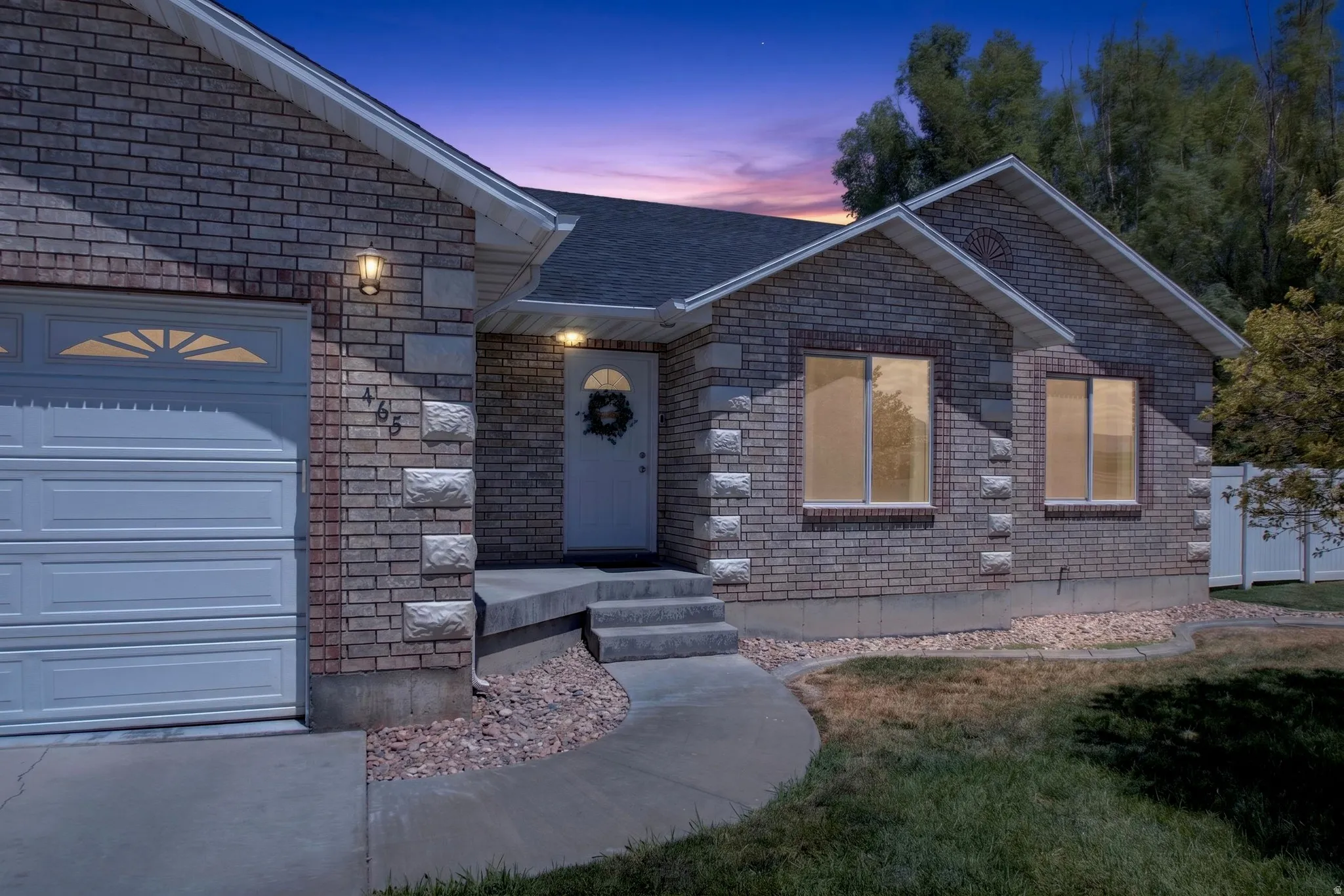 Brick and stone exterior featuring a covered entry, attached garage with decorative windows, and a paved walkway