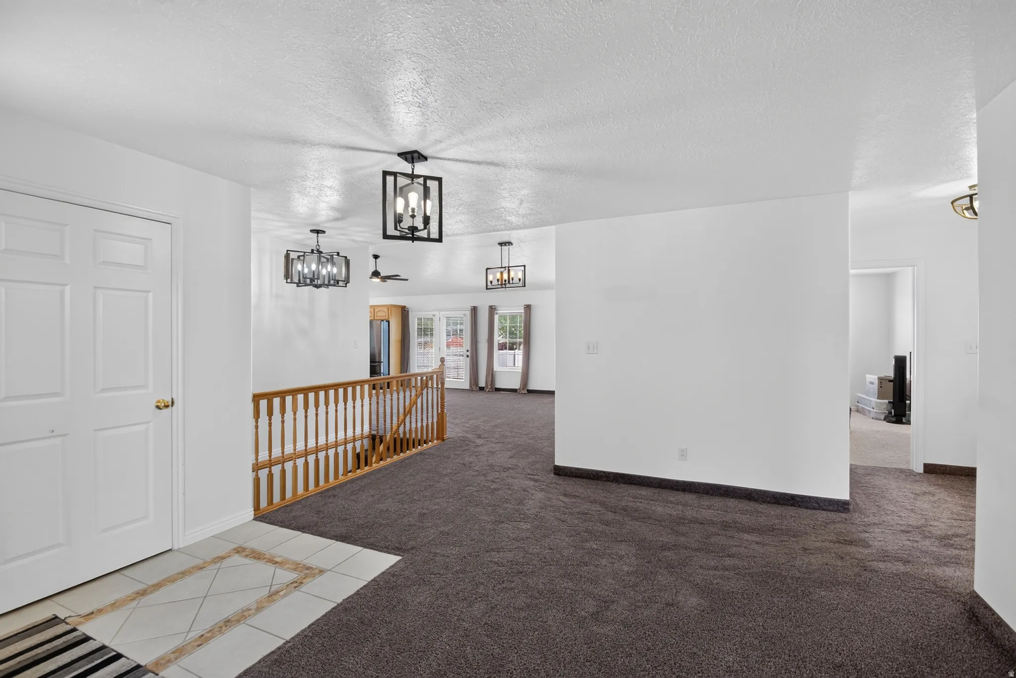 Entry area featuring a tiled floor inset, dark carpeting, and a wooden banister