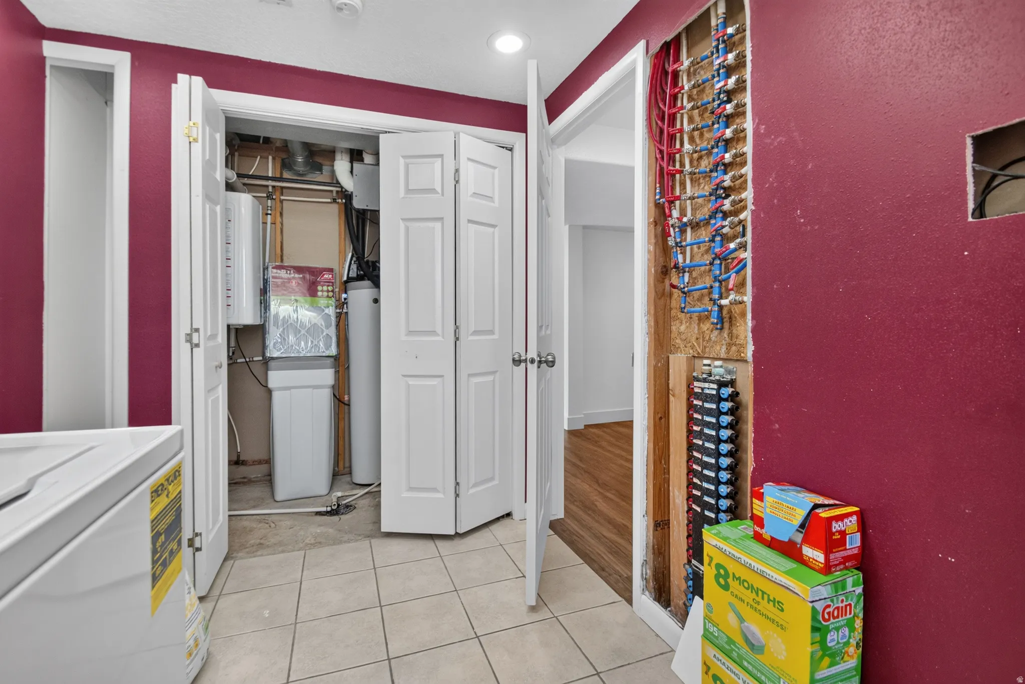 Utility area featuring a closed-door utility closet, exposed plumbing manifold, and light-toned tile flooring