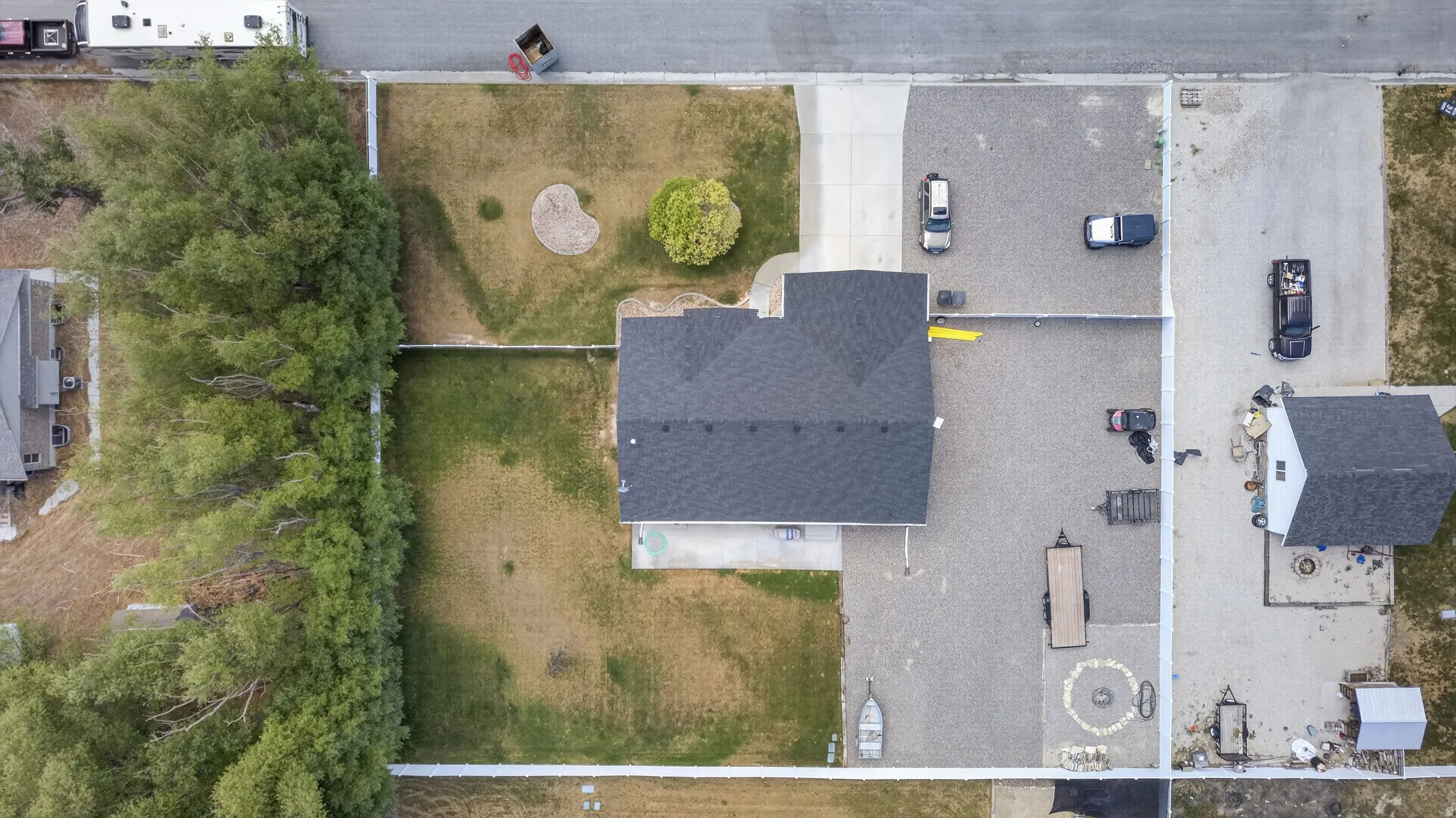 Aerial perspective showcasing a property with a dark shingle roof, a gravel parking area, and a separate outbuilding