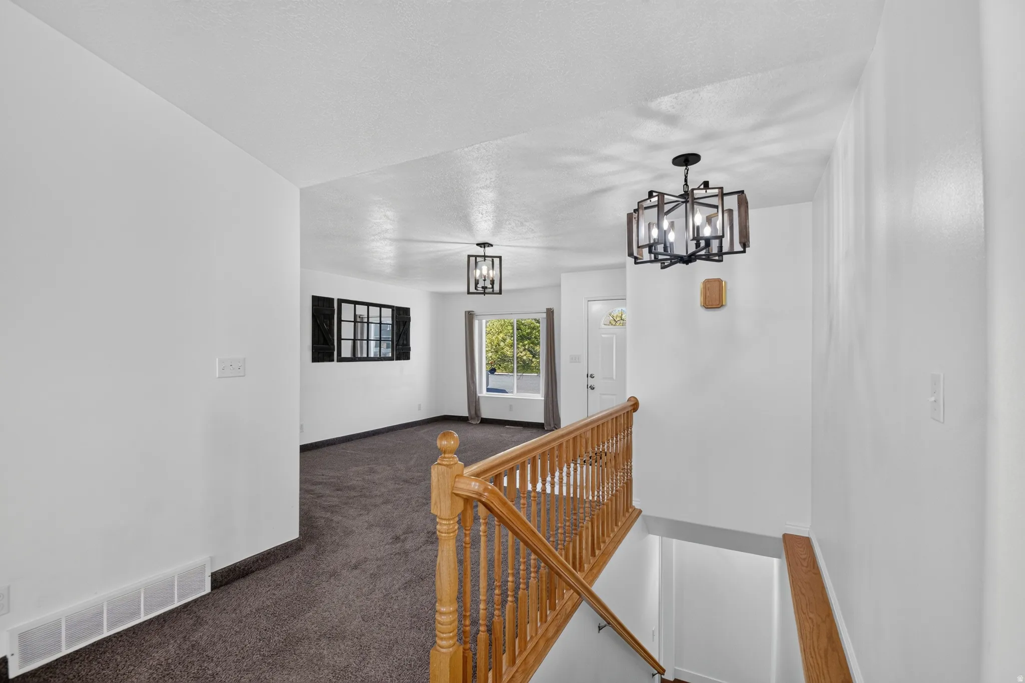 Split-level entry featuring a wood handrail and banister, dark carpet, and a modern chandelier