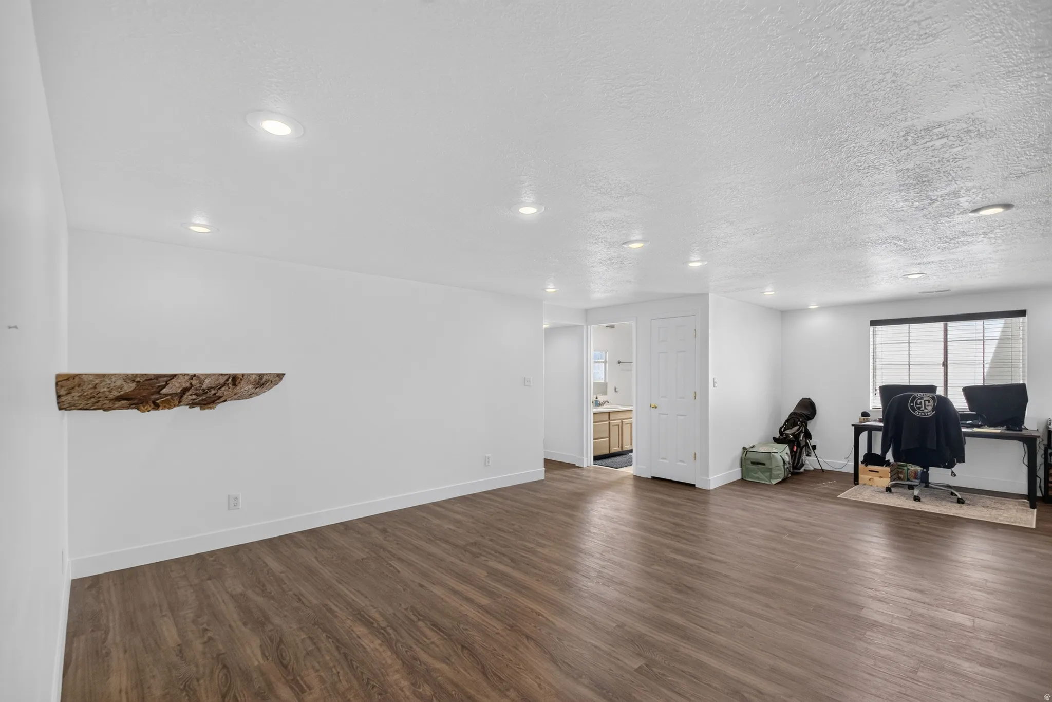 Spacious room featuring wood-finish flooring, recessed lighting, and a prominent floating wood shelf