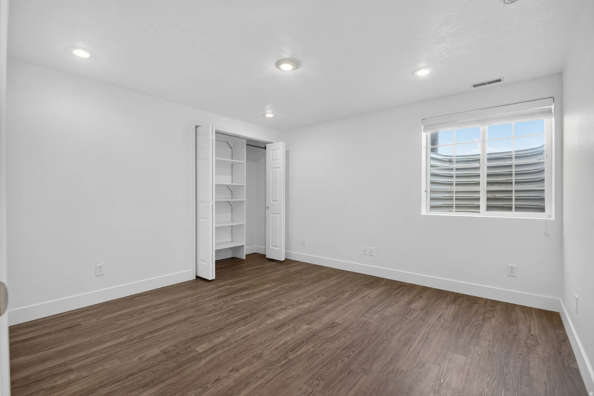 Spacious room featuring wood-finish flooring, white walls, and recessed lighting
