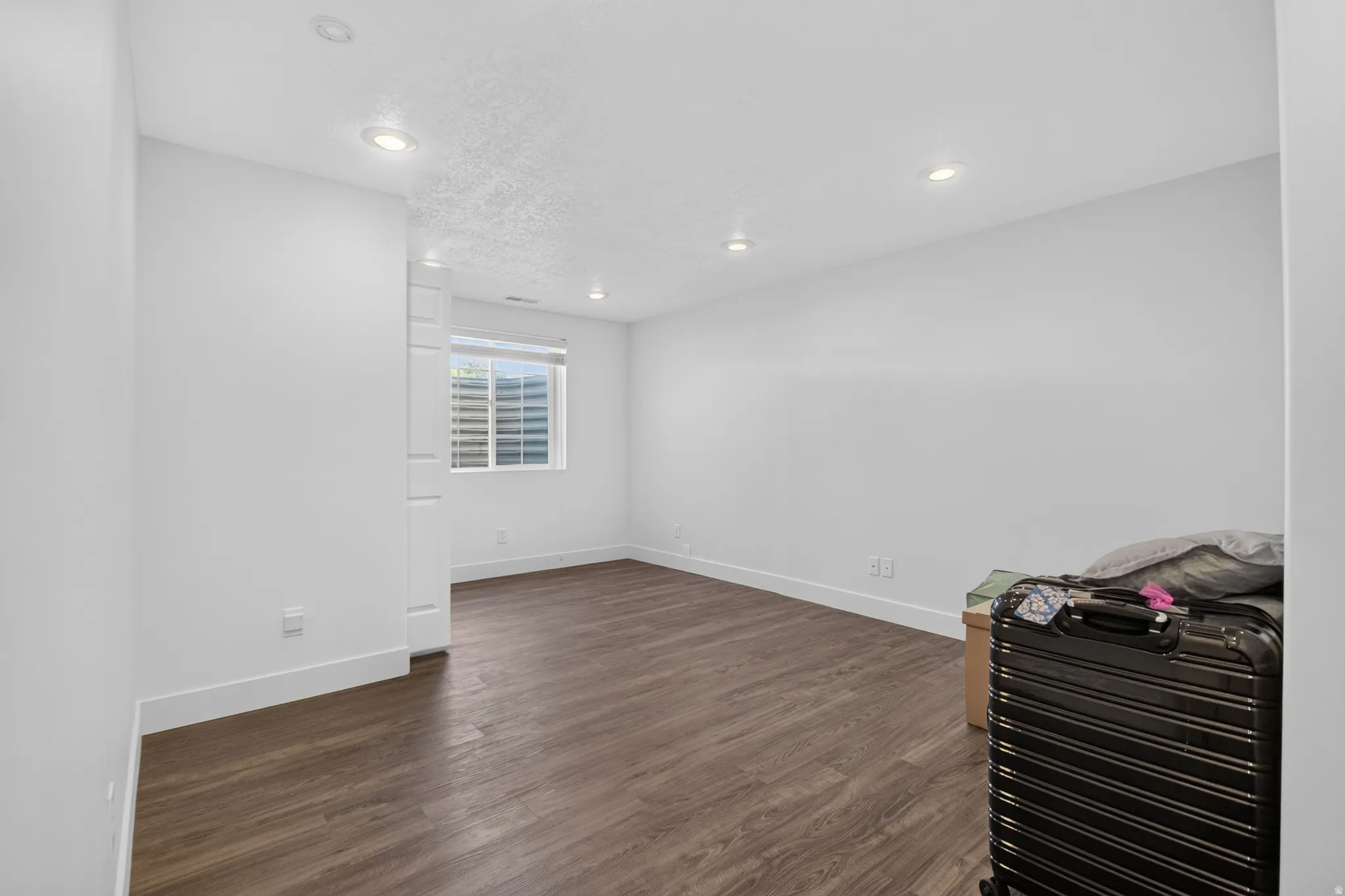 Spacious room featuring wood-finish flooring, recessed lighting, a white painted column, and a window with horizontal blinds