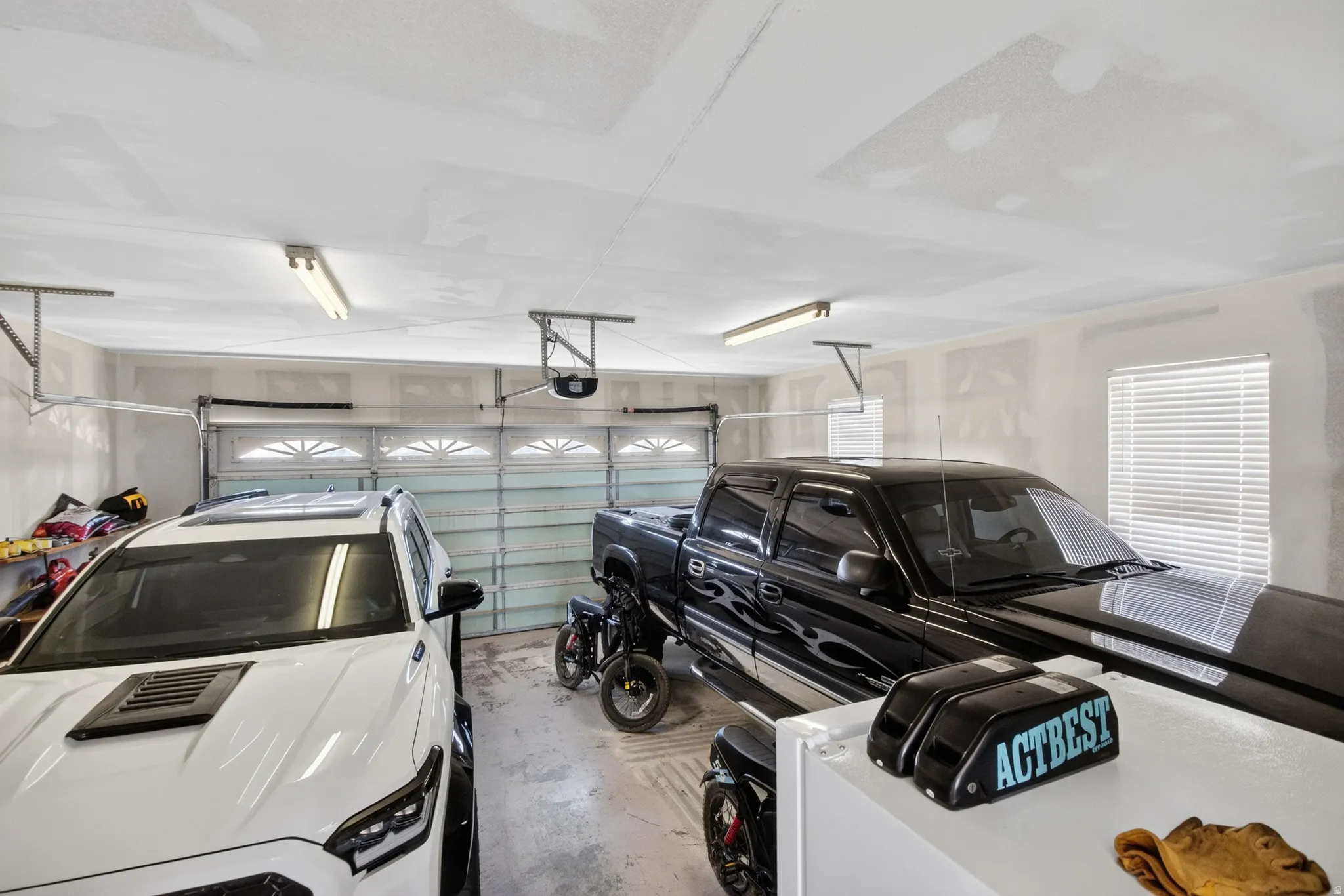 Two-car garage featuring overhead fluorescent lighting and a window with horizontal blinds