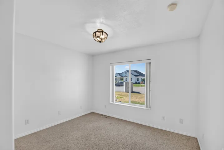 Carpeted room featuring a single window, white walls, and a ceiling-mounted light fixture