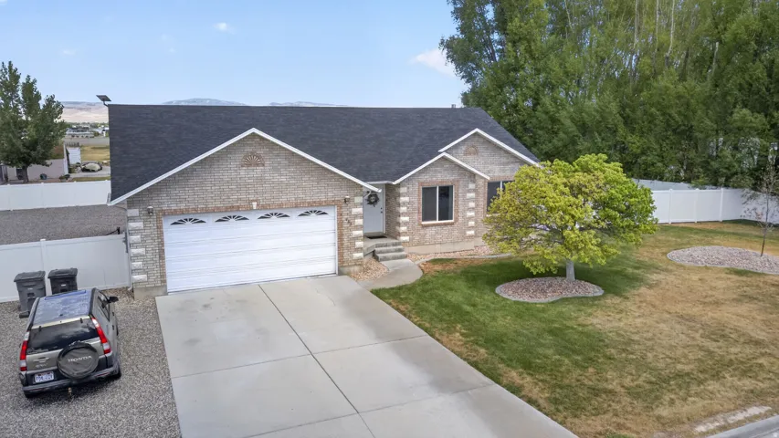 Brick exterior with a dark shingle roof, attached two-car garage, concrete driveway, and a front yard with mature landscaping