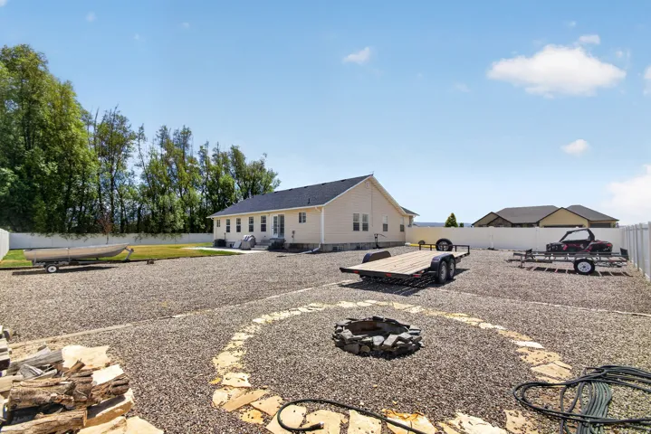 Expansive gravel backyard featuring a stone fire pit, bordered by a white privacy fence and mature trees