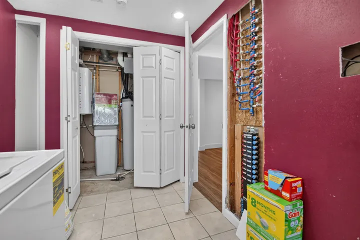 Utility area featuring a closed-door utility closet, exposed plumbing manifold, and light-toned tile flooring
