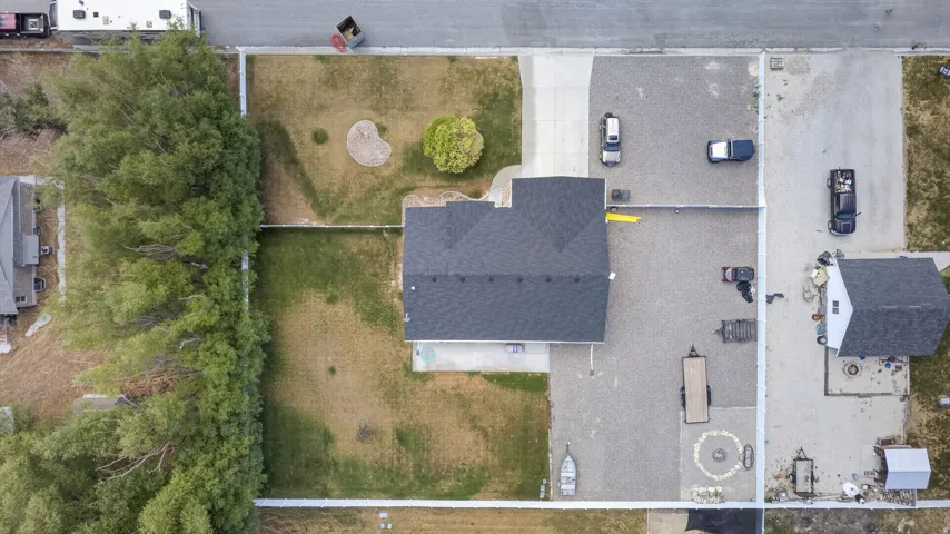 Aerial perspective showcasing a property with a dark shingle roof, a gravel parking area, and a separate outbuilding