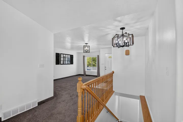 Split-level entry featuring a wood handrail and banister, dark carpet, and a modern chandelier