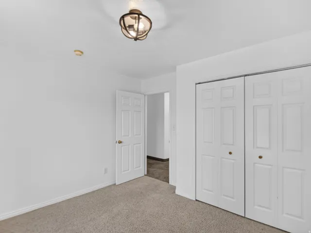 Carpeted room featuring a ceiling-mounted light fixture, white walls, and a pair of bi-fold closet doors with brass hardware