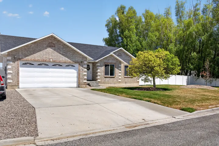 Brick facade residence featuring an attached two-car garage, mature front yard landscaping, and a white privacy fence