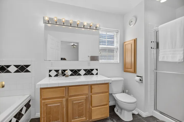 Light-filled bathroom featuring a wood-finish vanity with an integrated sink and tiled countertop