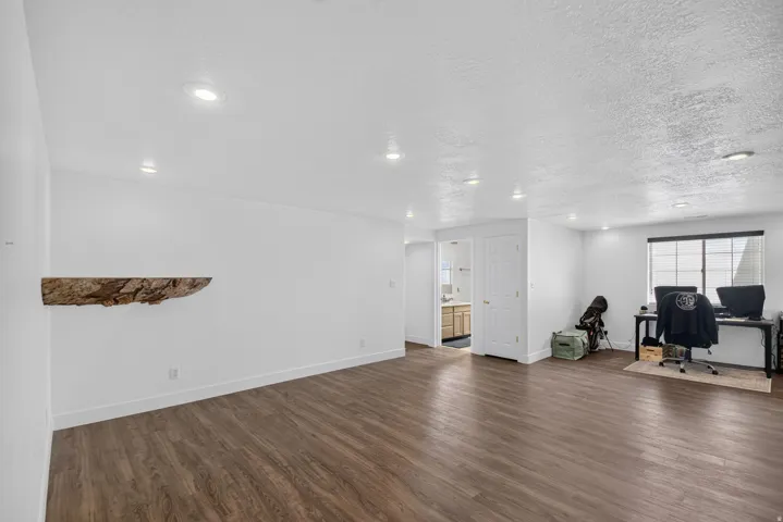 Spacious room featuring wood-finish flooring, recessed lighting, and a prominent floating wood shelf