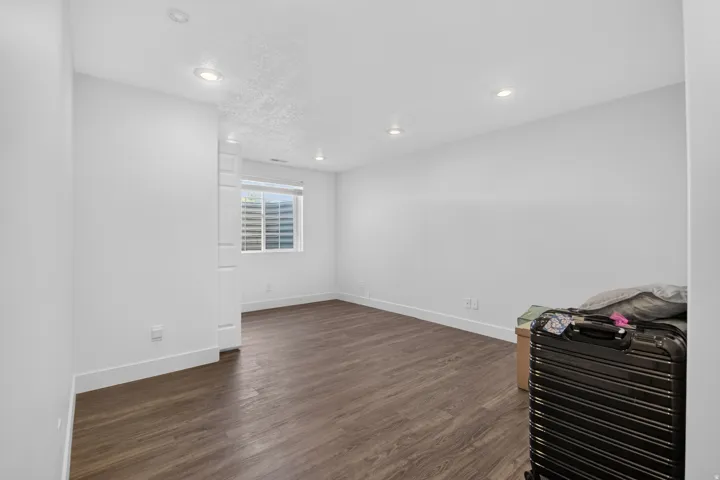 Spacious room featuring wood-finish flooring, recessed lighting, a white painted column, and a window with horizontal blinds