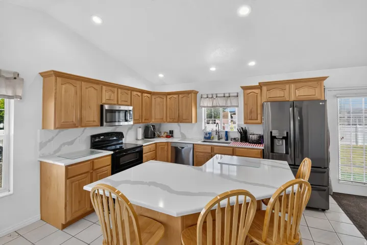 Kitchen featuring a large central island with seating, natural wood cabinetry, light-toned countertops with distinctive veining, stainless steel appliances, and recessed lighting