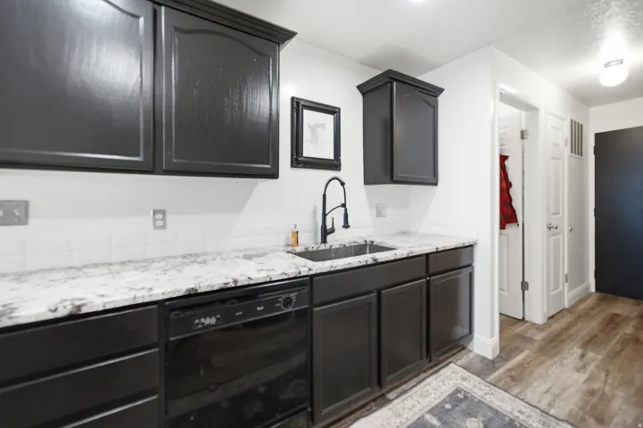Kitchen area featuring dark cabinetry, white countertops, white subway tile backsplash, and a stainless steel undermount sink with a matte black gooseneck faucet