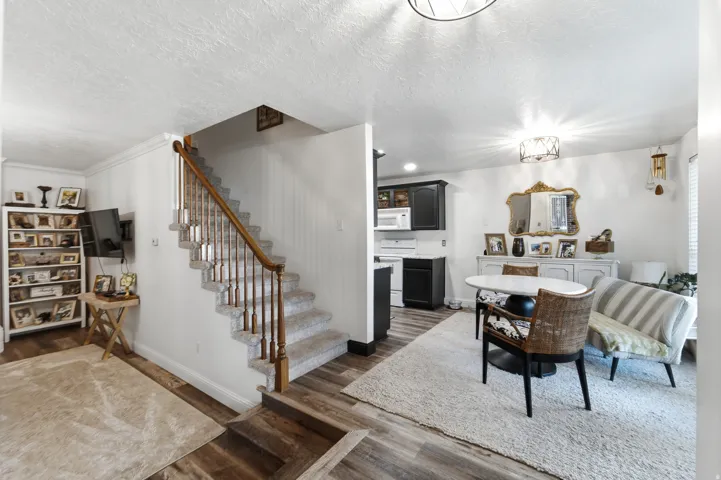 Open-concept living area with wood-finish flooring, a carpeted staircase with wood banister and balusters, and a dining space