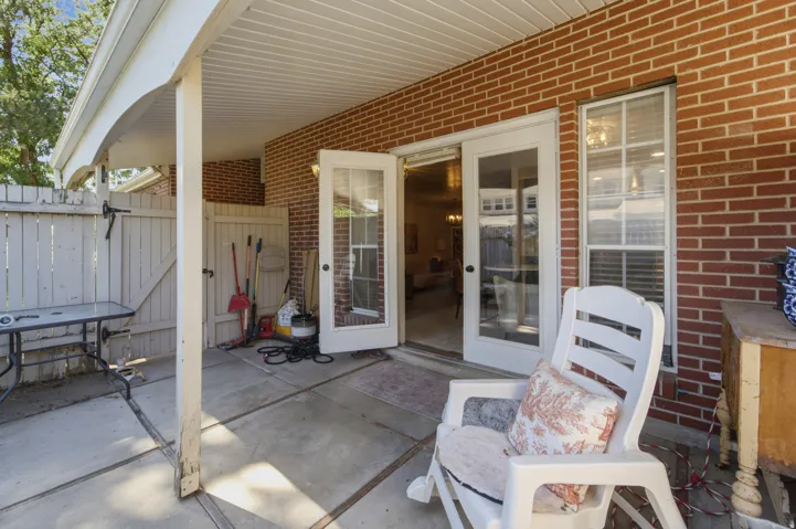 Covered patio area featuring a brick exterior wall, concrete flooring, white wood fence, and glass-paneled sliding doors