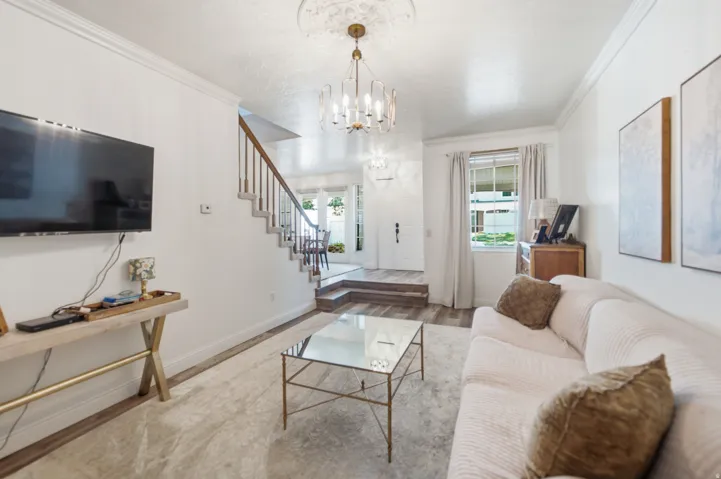 Bright living area featuring wood-finish flooring, a contemporary chandelier, and a staircase with a wooden handrail