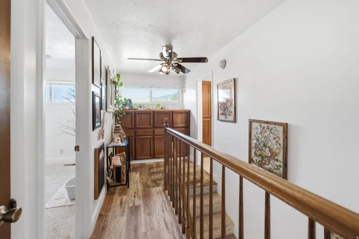 Upper-level hallway featuring wood-finish flooring, a ceiling fan, and built-in wood cabinetry with multiple windows above