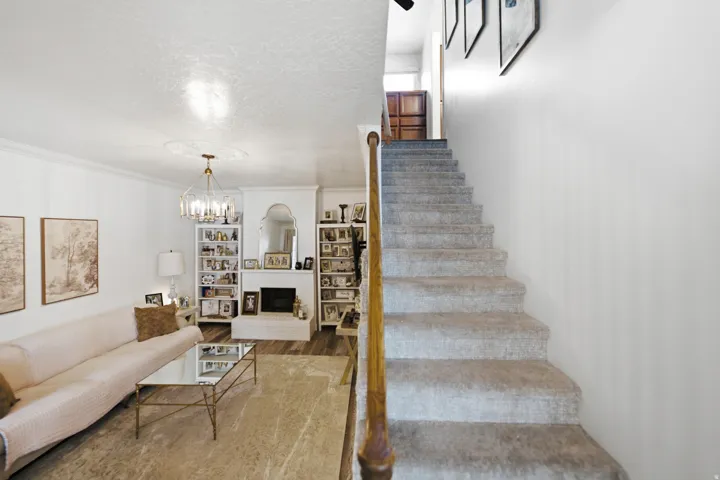 Living area featuring wood-finish flooring, a white fireplace with an arched mirror, built-in shelving, and a chandelier with a ceiling medallion
