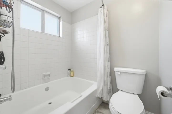 Bathroom featuring a white bathtub with white subway tile surround, a high-mounted window, and a white toilet