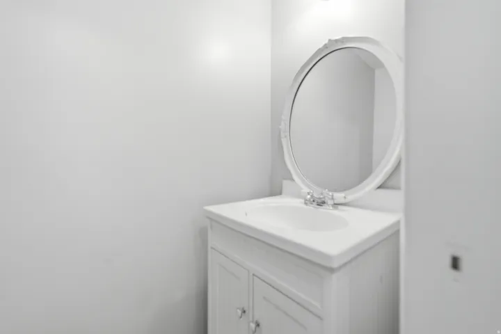 White vanity featuring an integrated sink, polished chrome faucet, and an ornate oval mirror