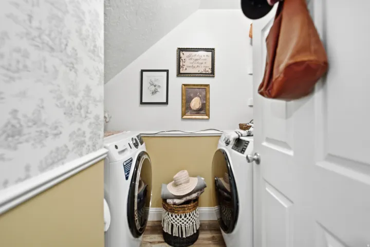 Dedicated laundry space featuring a white front-load washer and dryer set, wood-finish flooring, and a patterned accent wall